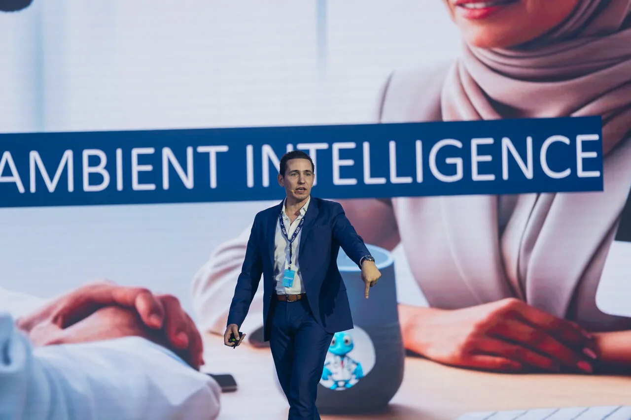 José Pedro Almeida walking the stage at a healthcare AI event in front of a screen reading Ambient Intelligence