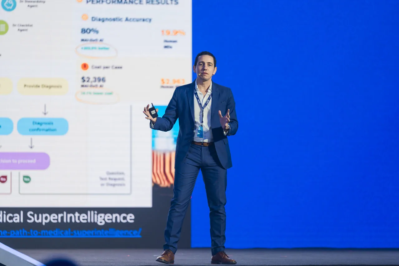 José Pedro Almeida on stage at a healthcare AI event, with a screen behind him showing diagnostic accuracy and per case cost metrics